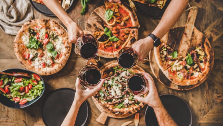 People clinking glasses with wine over table with pizza