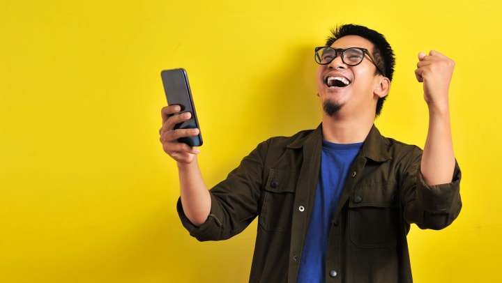 Man pumping his fist in the air and smiling while looking at his cell phone.