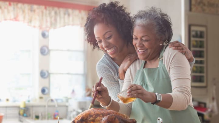 Younger woman and older woman smiling in a kitchen while basting a turkey