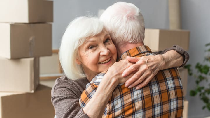Senior couple hugging with moving boxes in the background.