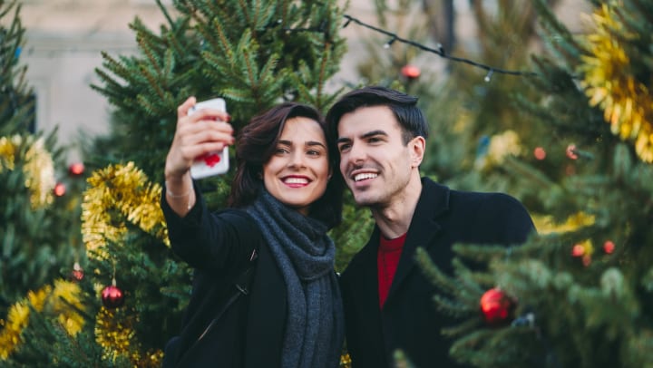 A man and a woman taking a selfie surrounded by Christmas trees.