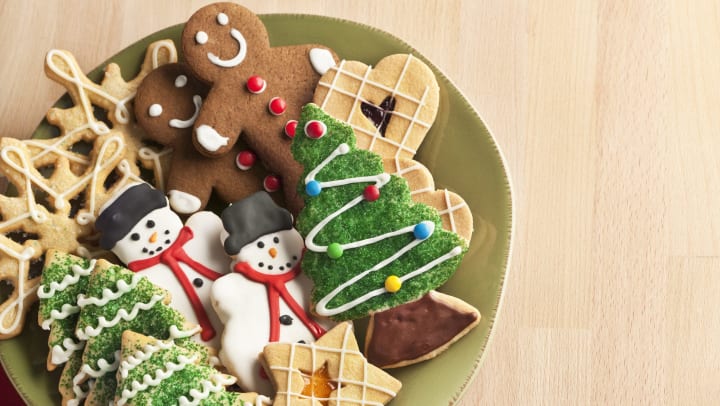 A plate with Christmas tree sugar cookies, frosted snowman cookies, thumbprint cookies, and gingerbread men. 