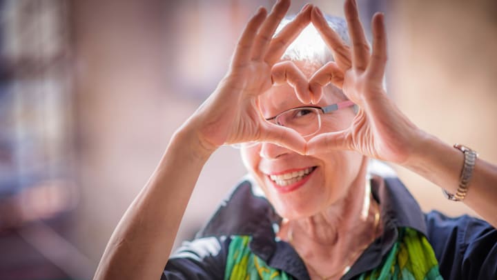 Woman smiling and making a heart shape out of her fingers