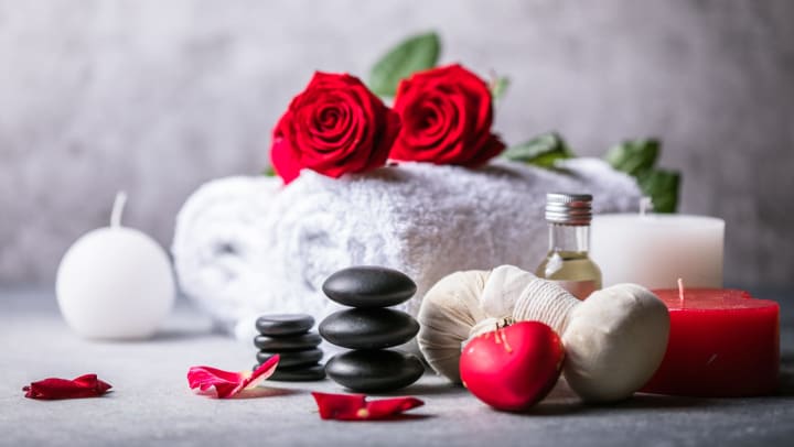 Red roses on top of rolled towels with candles and massage stones in front of them.