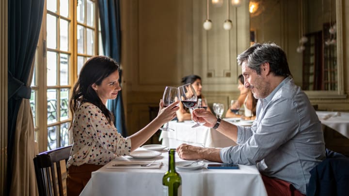 Man and woman in a restaurant, toasting wine glasses over a dining table 