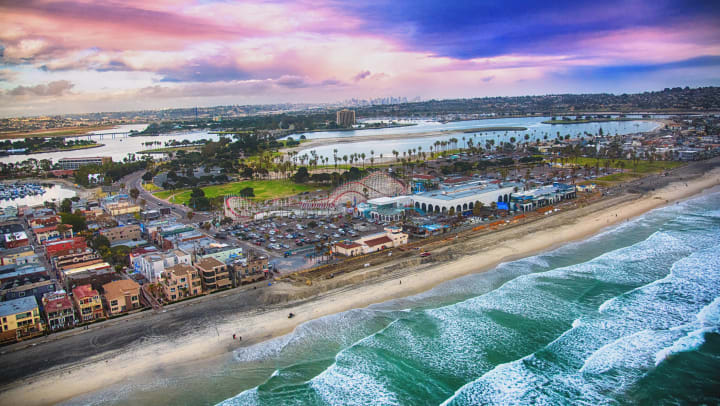 The iconic Big Dipper roller coaster at Belmont Park featured in the center of this aerial photograph of Mission Beach in San Diego, California. The downtown skyline is visible in the distance.