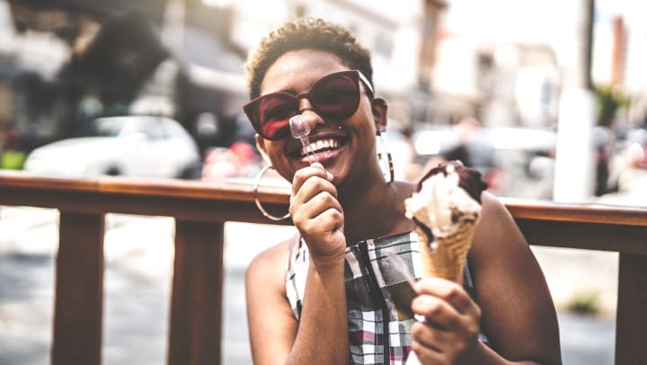 Woman outside holding a clear spoon and ice cream cone and smiling.
