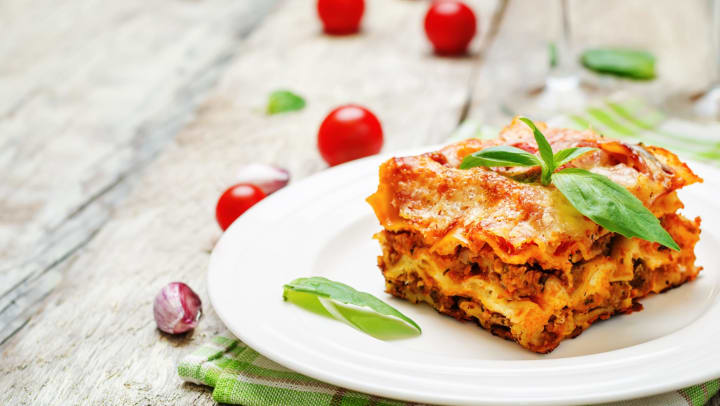 Plated slice of lasagna on a white wood background.