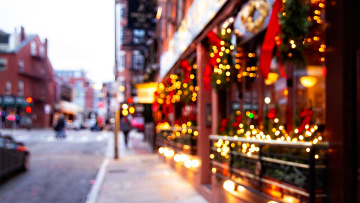 A blurry image of a sidewalk with storefronts decorated for the holidays.