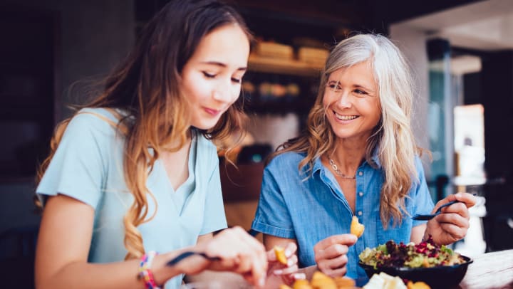 A young adult woman and middle-aged woman eating together in a restaurant.