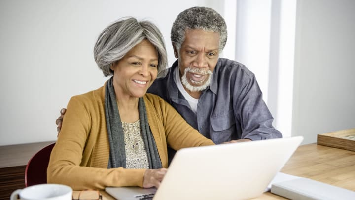 Senior couple looking at laptop together at home. The woman is typing and the man is watching with his arm around her at Brightwater Senior Living of Tuxedo in Winnipeg, Manitoba