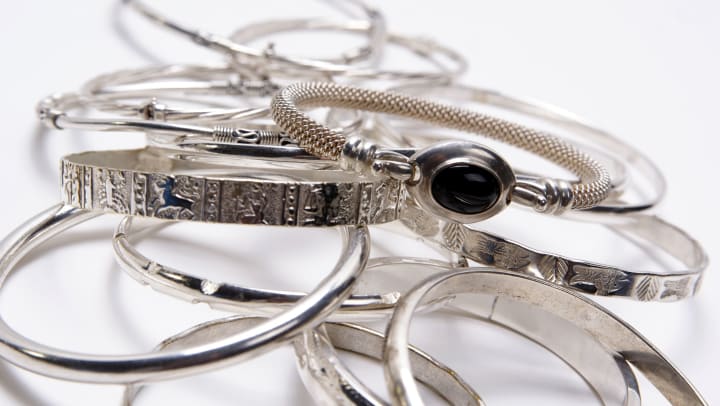 A pile of silver bracelets on a white background. 