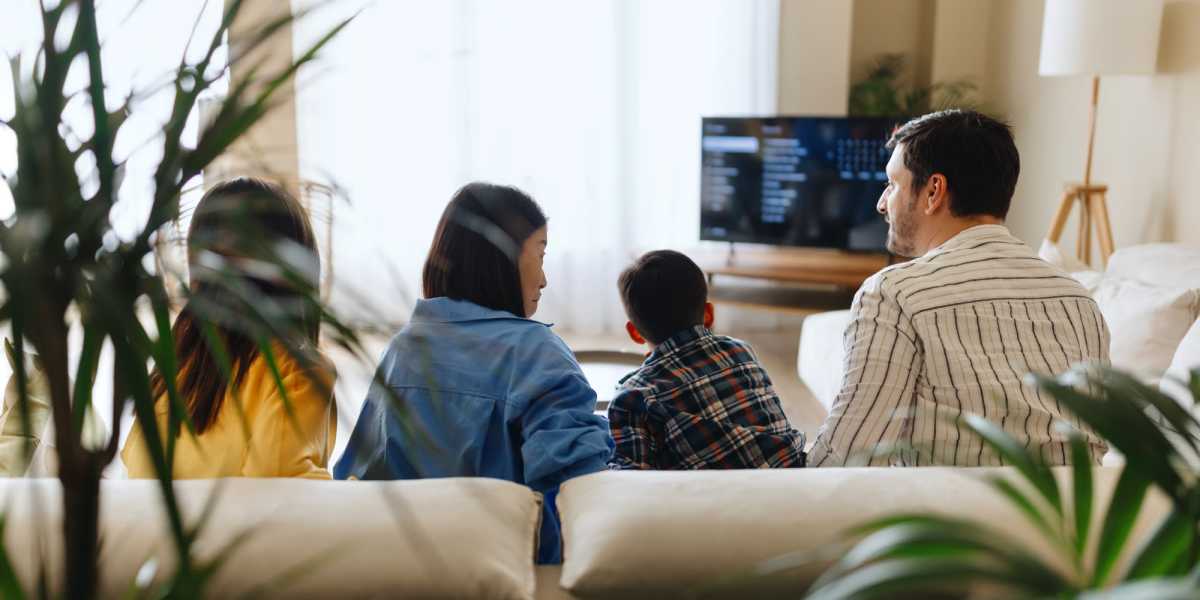 Family sitting on a couch watching television at Avia Lofts at Maple Road in Amherst, New York