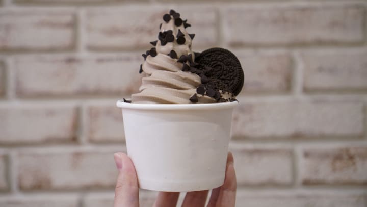 A yogurt soft ice cream chocolate flavor topped with chocolate chips and cookie.