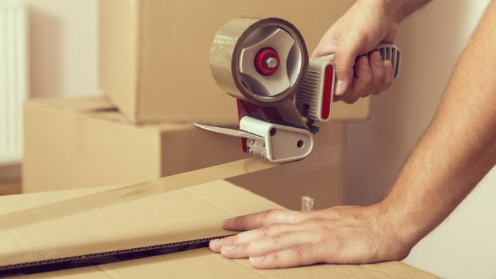 Packing tape being used on a box with a hand on the box.
