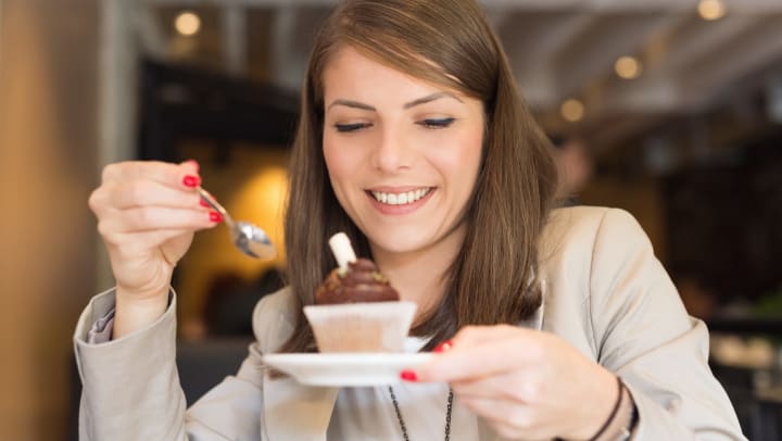 A woman smiling as she eats a cupcake with a spoon.
