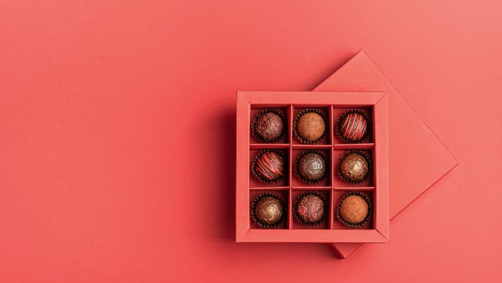Chocolate candies in a red craft box on a bright coral background.