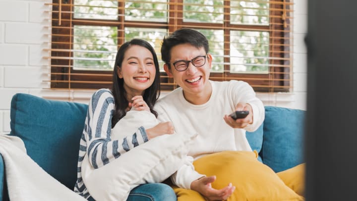 Young couple sitting on a blue couch and laughing while watching television