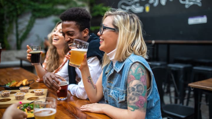 A group of smiling friends having fun while laughing and drinking beer on an outdoor patio.