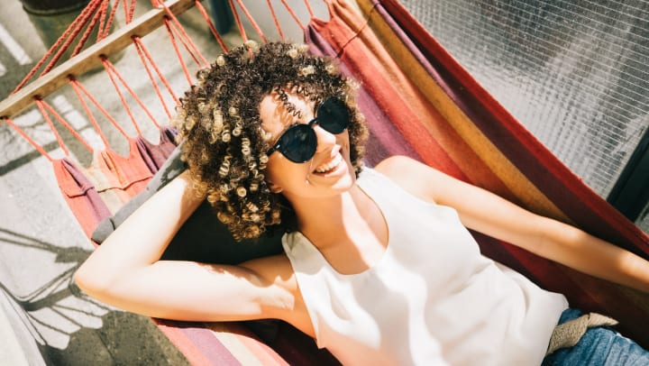 A smiling woman relaxing in a hammock on her balcony in the sunshine.