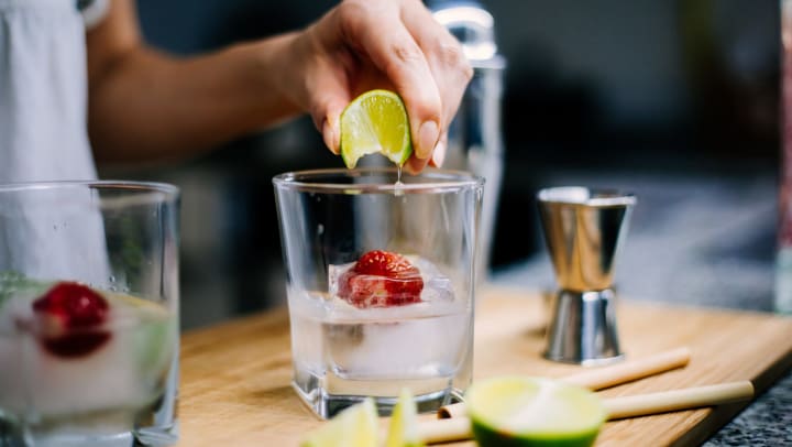 Person squeezing a lime into a glass containing ice and a strawberry.