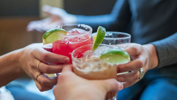 Close up of three people toasting fancy drinks in rocks glasses