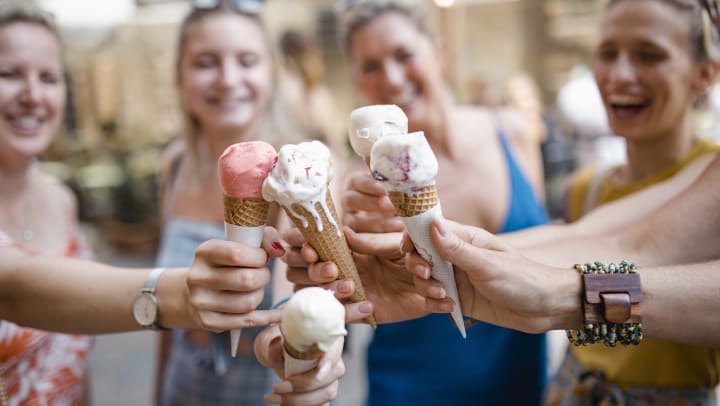 A group of women smiling and holding up their ice cream cones together.