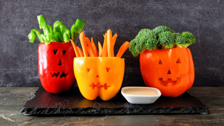 Jack-o’-lantern bell peppers filled with chopped veggies next to a bowl of dip.