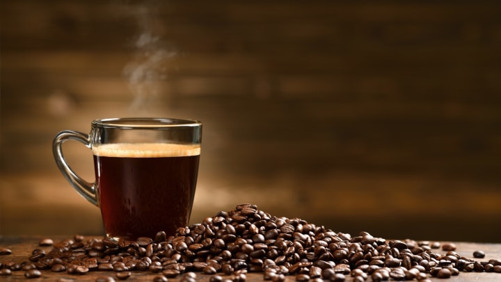 Glass cup of coffee and coffee beans on old wooden background