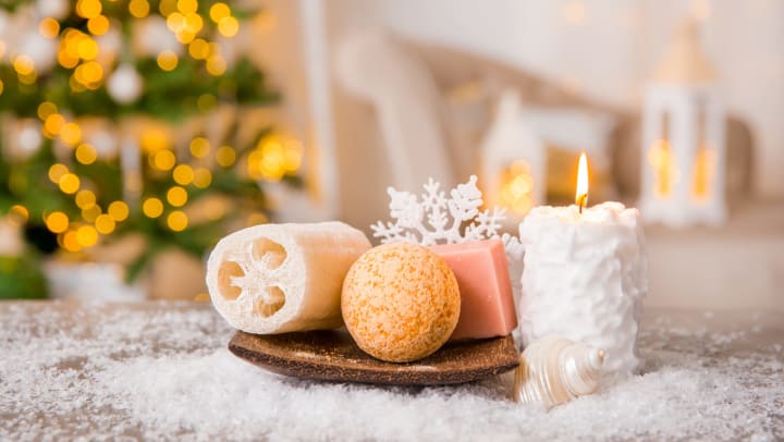 A white candle and assortment of soaps in a bright white interior with a lighted tree in the background