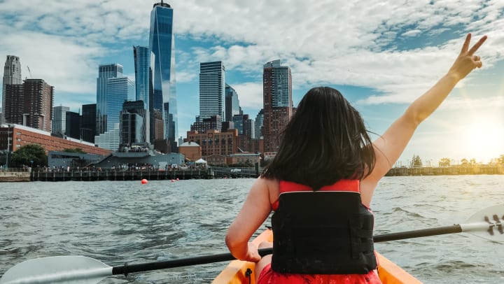 A woman kayaking the Hudson in New York City, holding up her hand in the peace sign.