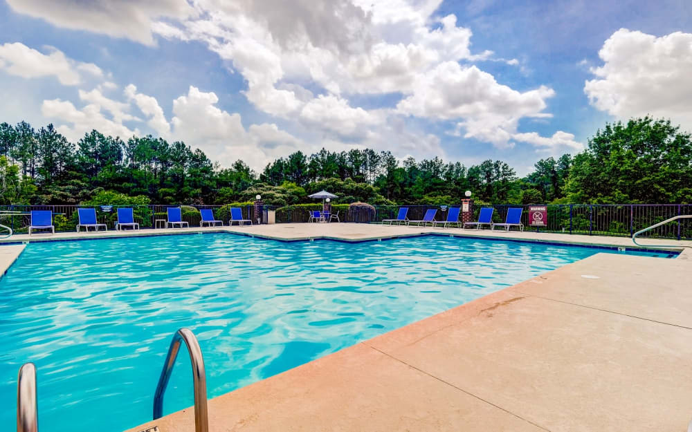 Swimming pool with poolside tables with umbrellas and lounge chairs at Chason Ridge Apartment Homes in Fayetteville, North Carolina