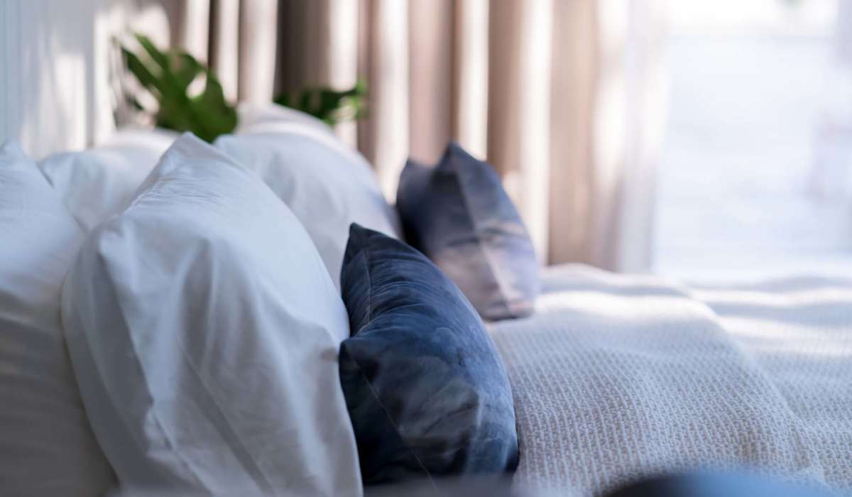 A white bed adorned with blue pillows beside a window at Granite Creek, Rocklin, California.