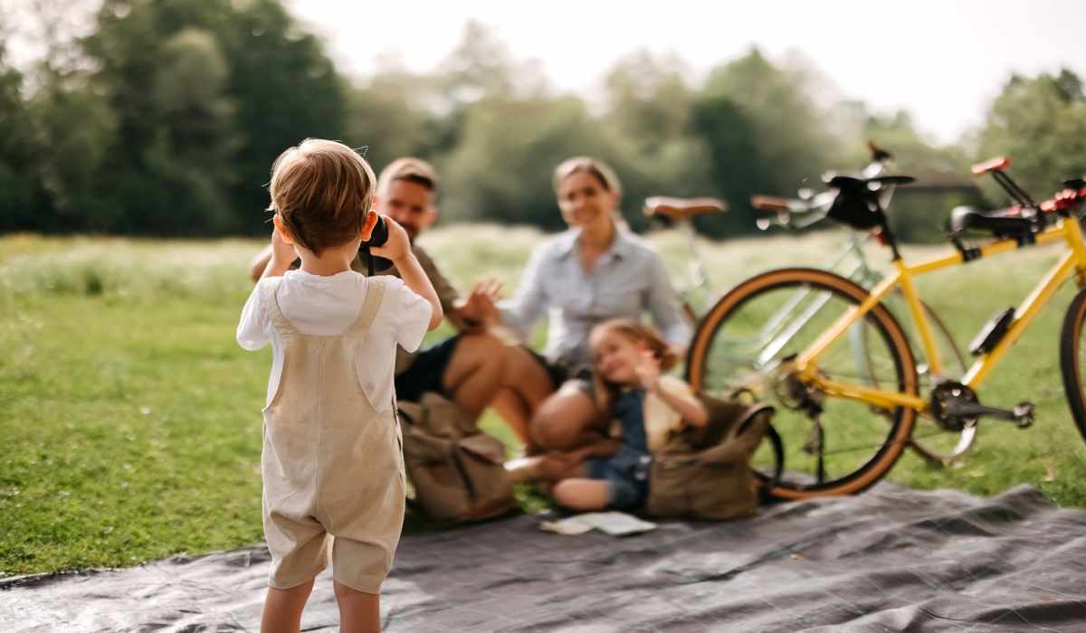 Child taking photo of family on picnic blanket with bicycles nearby and greenery in background at Pleasant View Townhomes in Baltimore, Maryland 