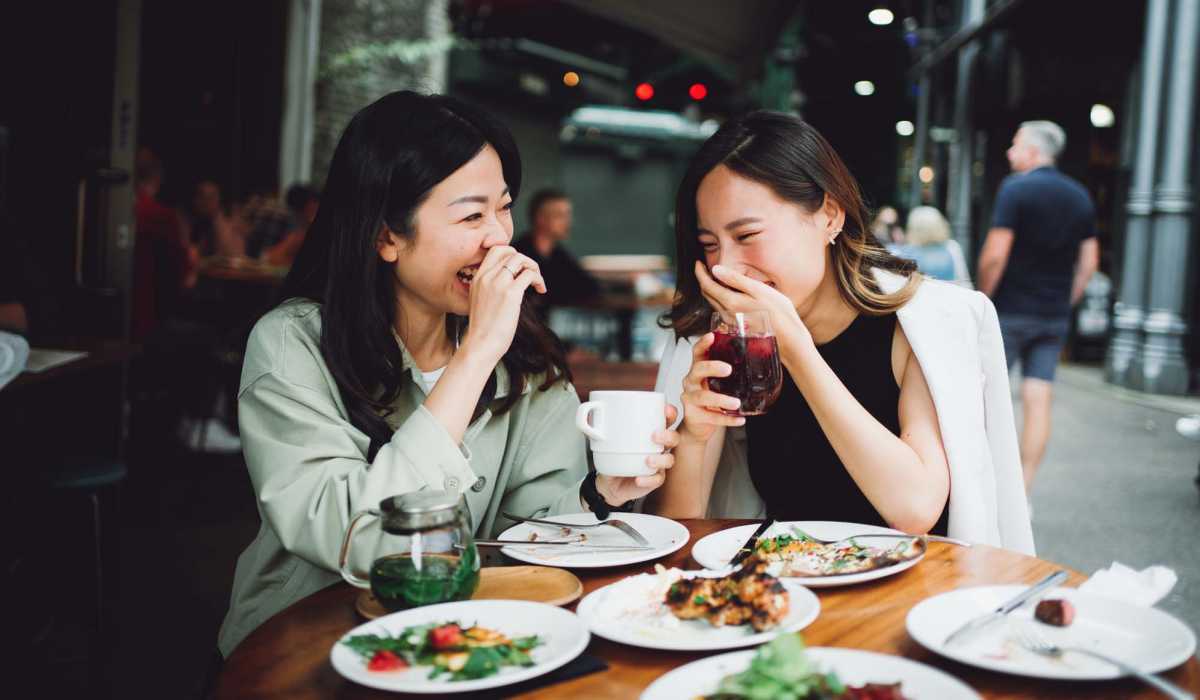Two women laughing over a table of food near Collins Crossing Apartments in Carrboro, North Carolina 
