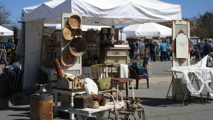 Antique chairs, baskets, and other furniture for sale displayed under a white tent