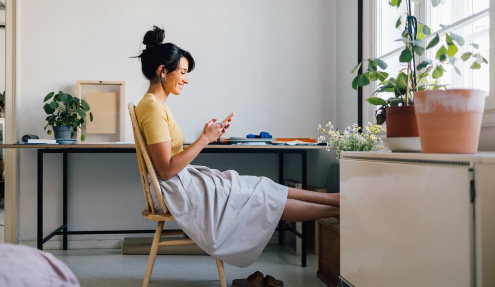 Woman relaxing with phone in bright room at 4500 Dewey Ave Apartments in Rochester, New York 