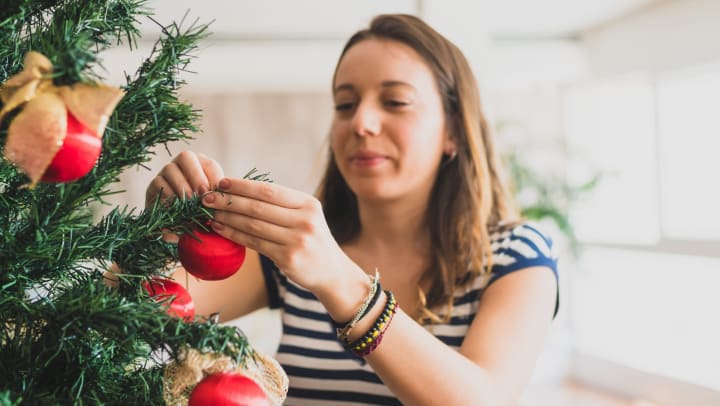Young woman smiling while putting ornaments on a holiday tree.