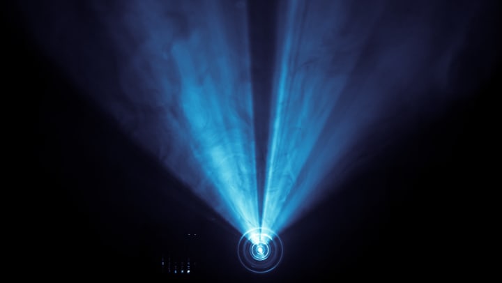 A projector shines a spotlight through a smoky texture in a dark space.