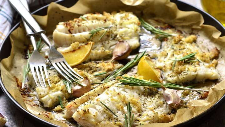 Baked cod with ginger, lemon, and rosemary on a parchment paper lined tray.