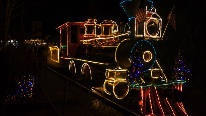 Holiday lights outlining a train locomotive with American flags on it.