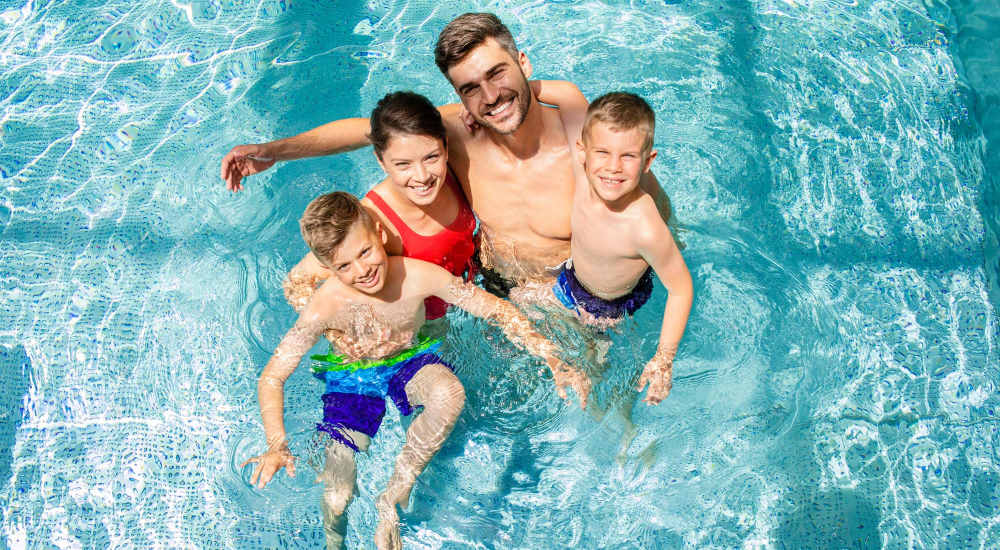 Resident couple swimming with two children in pool at Canandaigua Lake Apartments in Canandaigua, New York