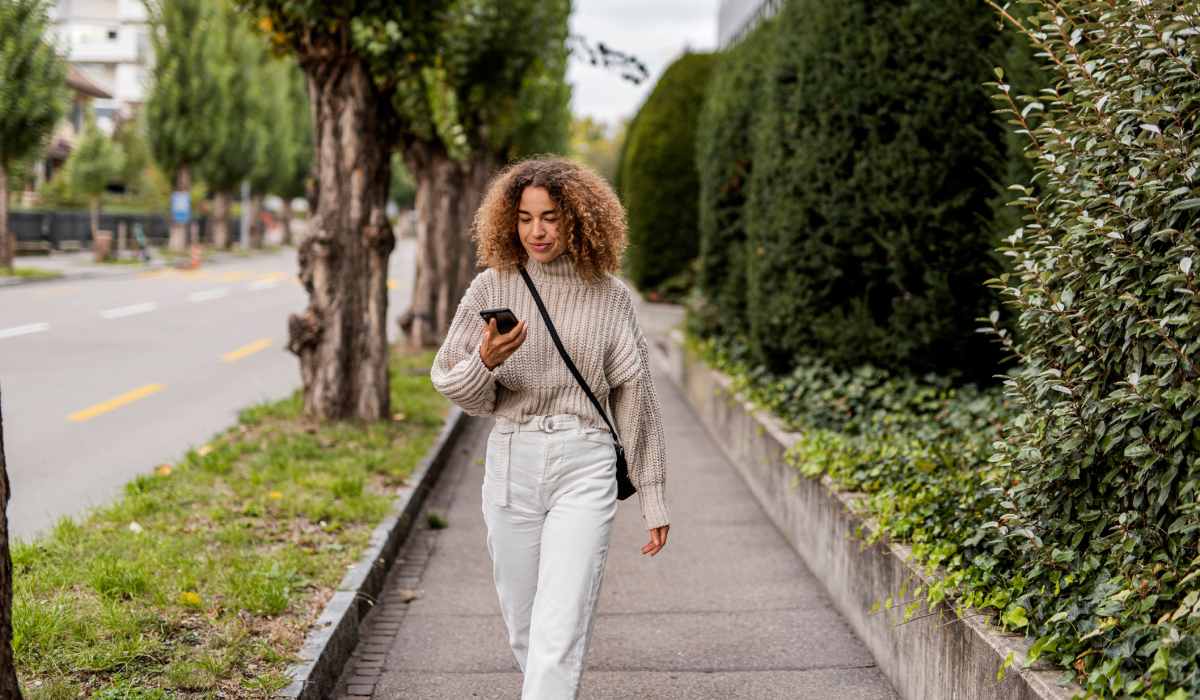 Resident woman walking in the street while holding her phone near Mirada Apartments in Lewis Center, Ohio