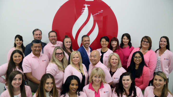 Twenty-three Liberty team members wearing pink clothing pose for a photo in front of the Liberty flame icon sign.