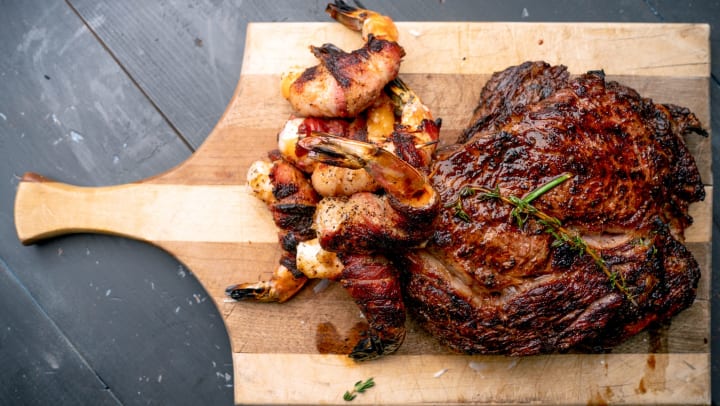 Giant ribeye steak on a cutting board with bacon wrapped prawns. 