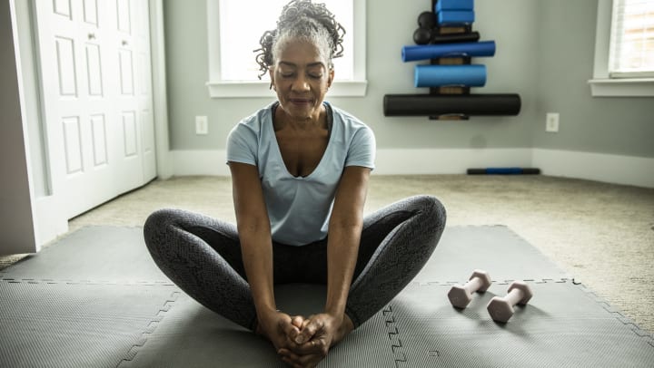 Senior woman sitting in a yoga pose on a mat.