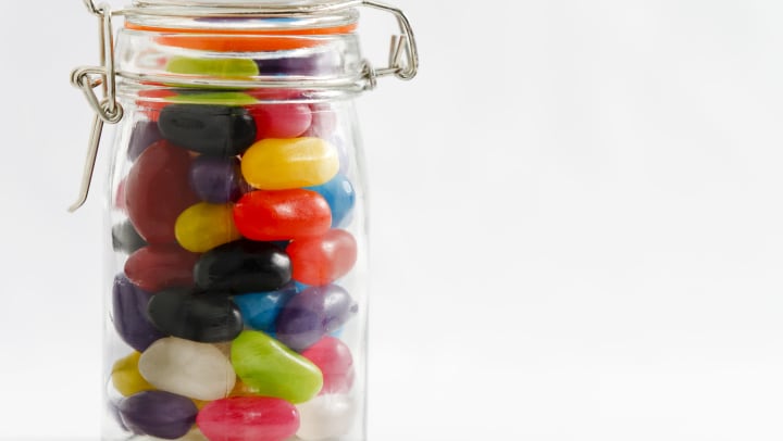 A clear jar full of colorful jelly beans on a white background. 