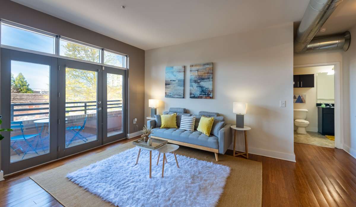 A brightly lit living room with a blue sofa and large windows lead to a balcony with a table at Attain Shockoe, Richmond, Virginia