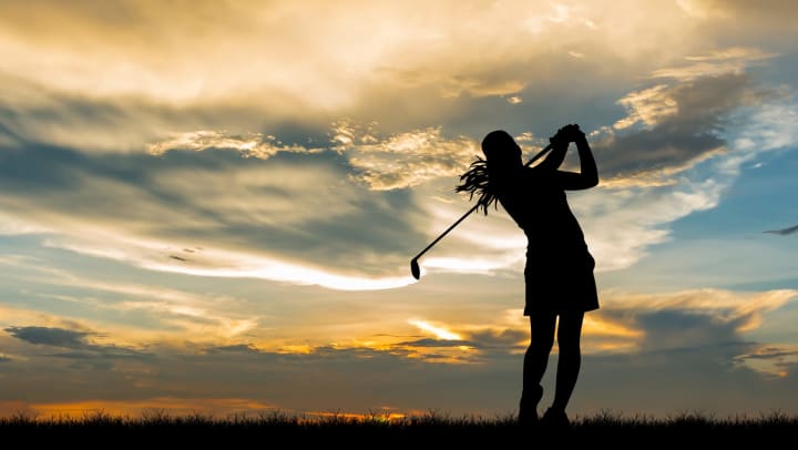 The silhouette of a female golfer at the end of her swing. 