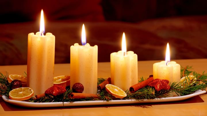 A pretty centerpiece with four pillar candles, evergreens, lemon slices, and cinnamon sticks on a rectangular tray. 